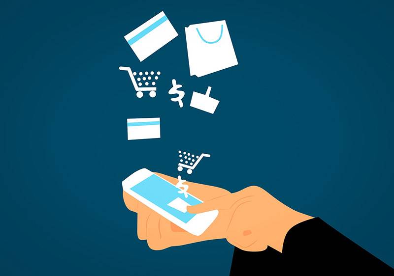 An individual holding a phone with various icons popping out of it including a shopping cart and credit card illustrating the role ecommerce solutions play in our daily lives.